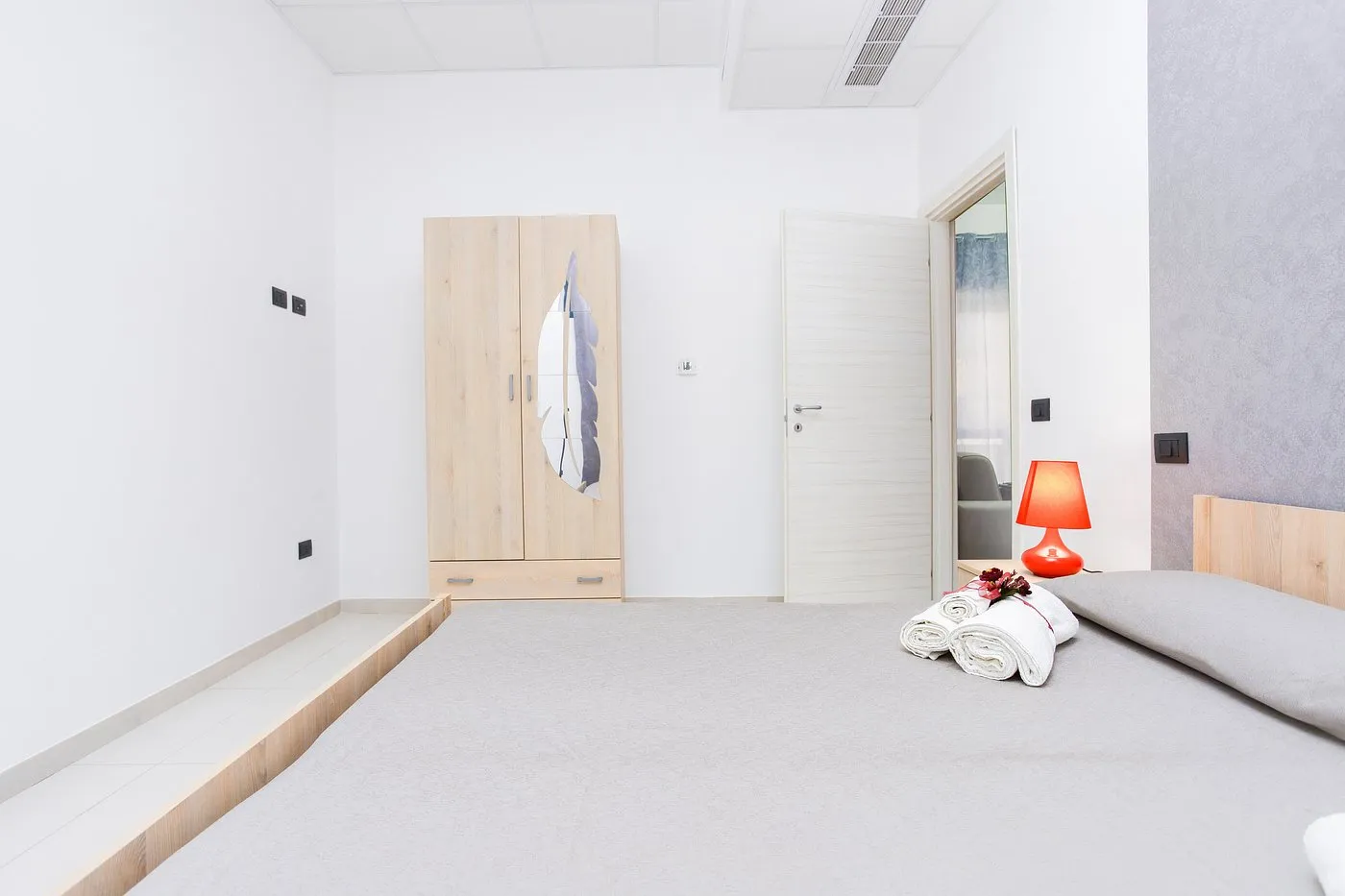 Camera spaziosa con armadio in legno, letto matrimoniale e lampada rossa