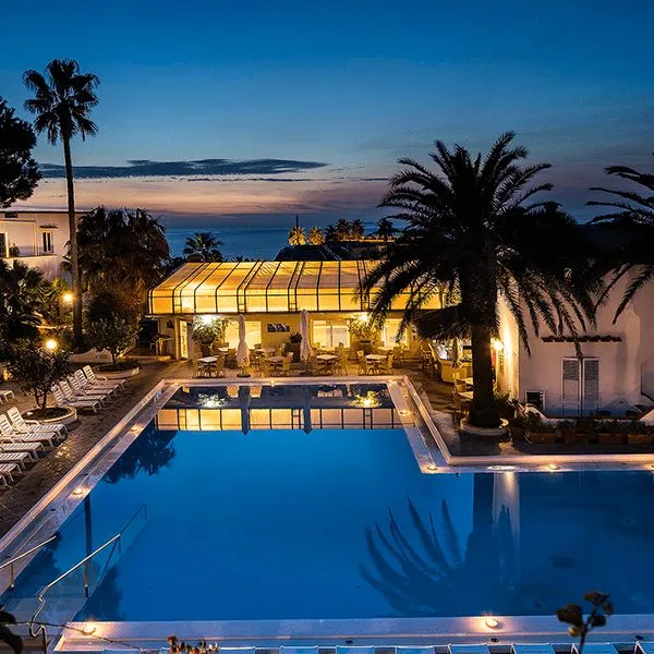 Vista serale della piscina illuminata con palme e veranda in vetro al tramonto