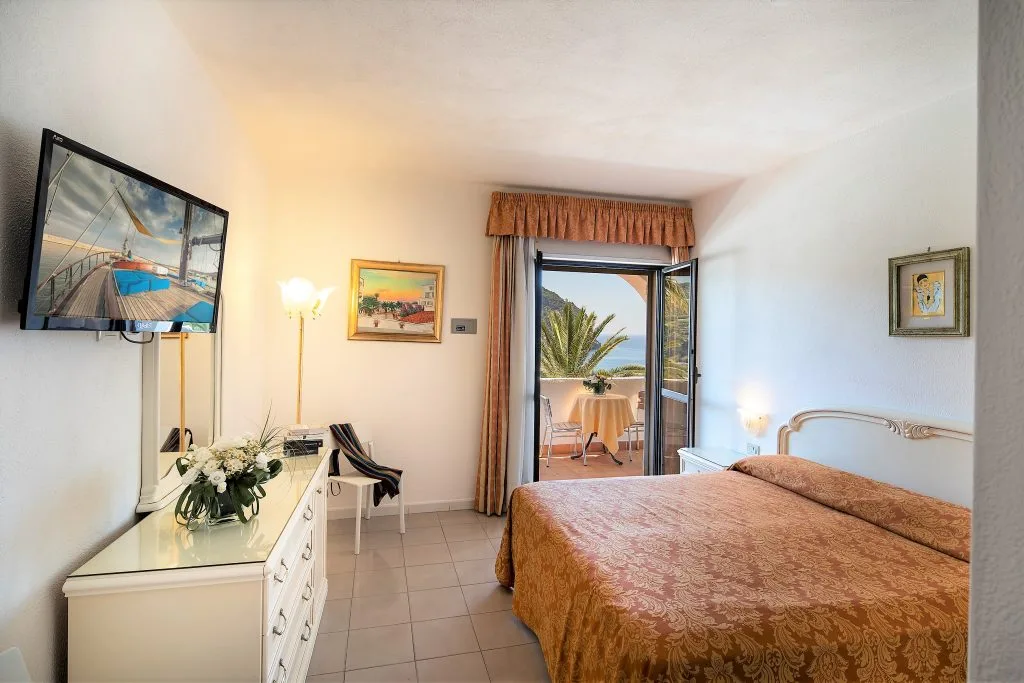 Camera matrimoniale elegante con TV, comò bianco e balcone con vista mare