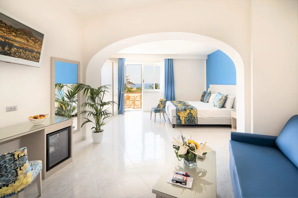 Ampia camera luminosa in stile mediterraneo con arco, divano blu e balcone vista mare