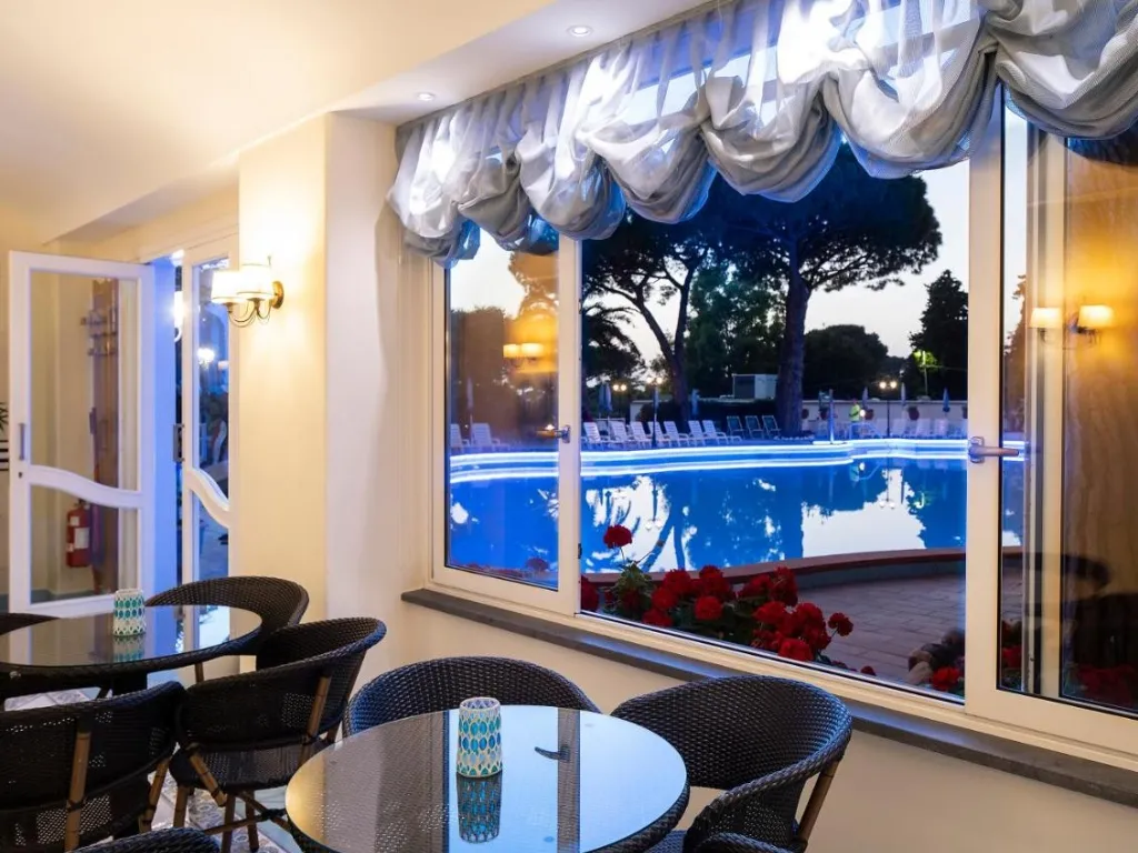 Sala interna con tavoli e vista sulla piscina illuminata attraverso le finestre