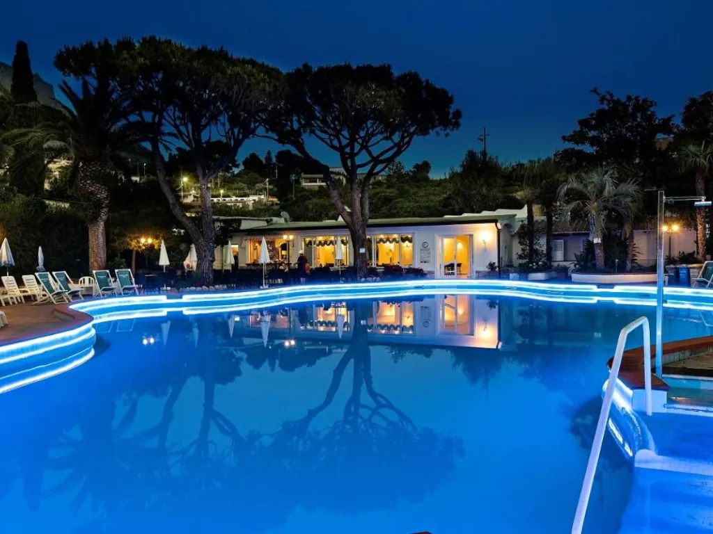 Piscina illuminata di sera con luci blu e ristorante dell'hotel sullo sfondo