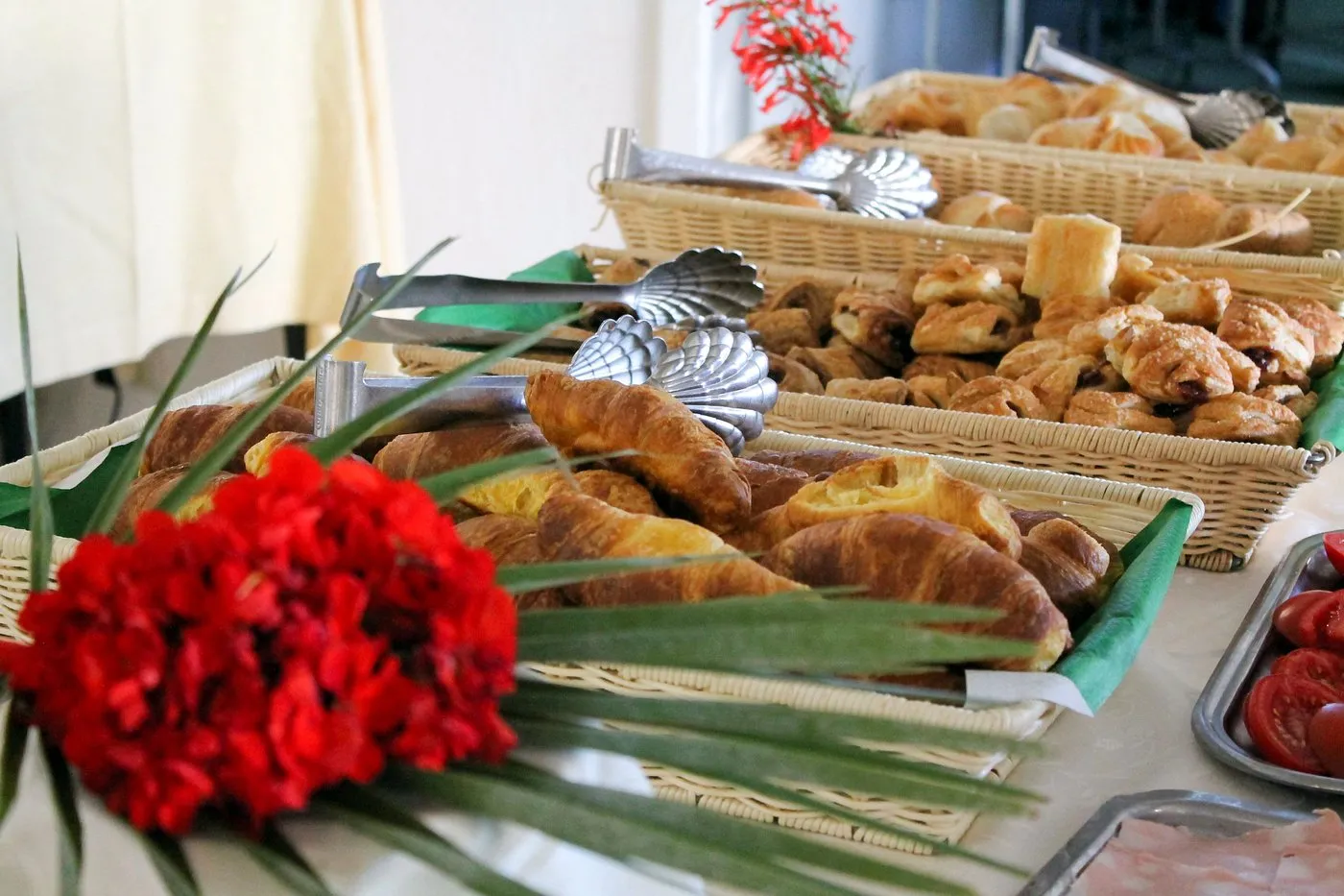 Buffet di colazione con cornetti e dolci in cestini di vimini e fiori rossi