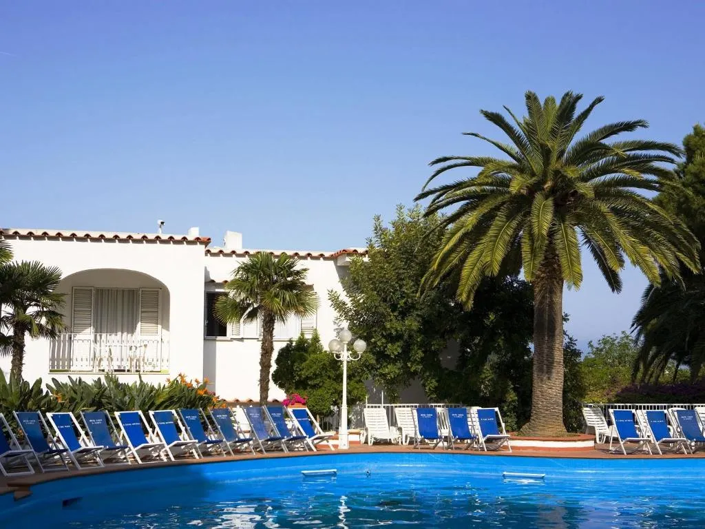 Piscina esterna con lettini blu e palme accanto all'edificio bianco dell'hotel