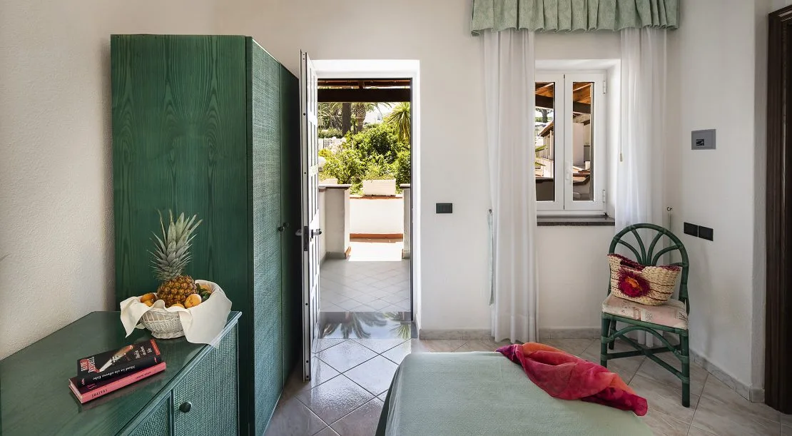 Camera con armadio verde, comò e accesso alla terrazza sul giardino