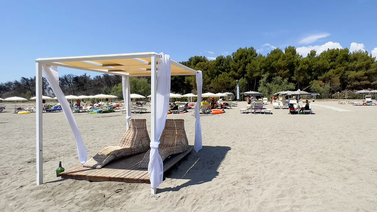 Lettino baldacchino in vimini con tende bianche sulla spiaggia attrezzata