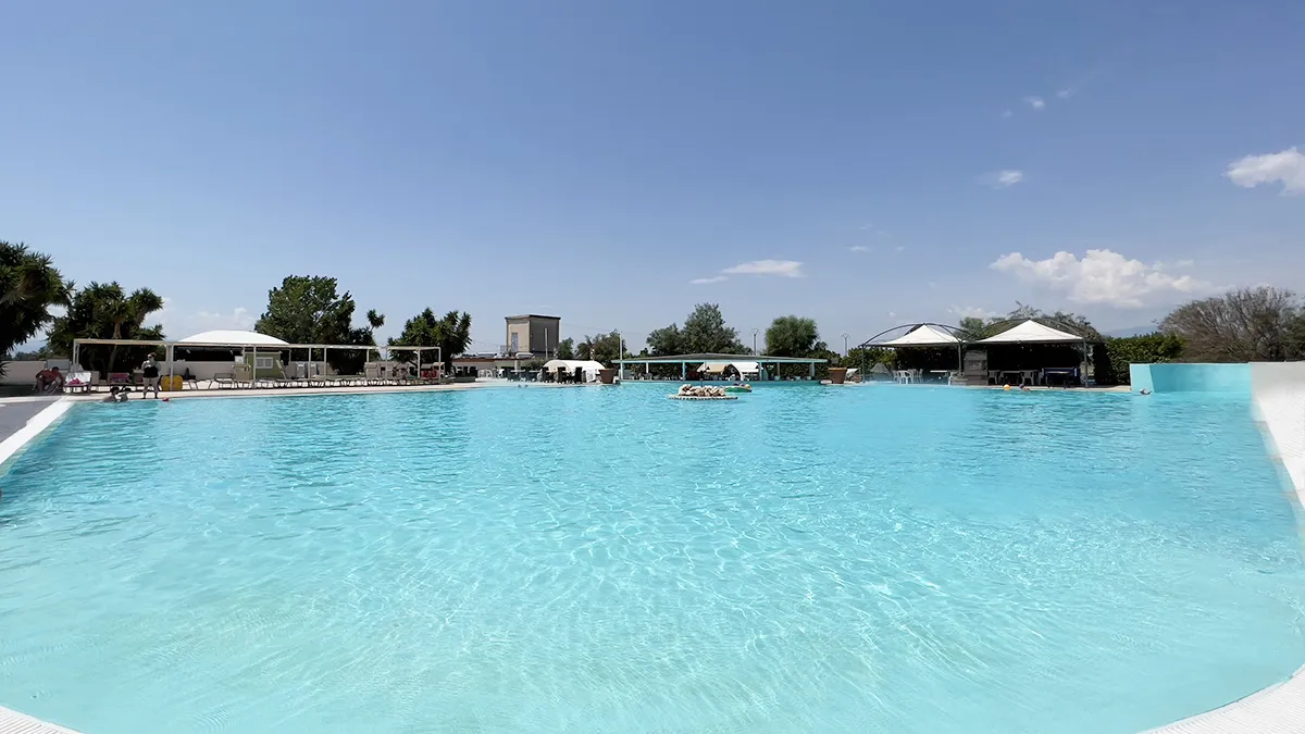 Grande piscina con acqua cristallina, gazebo e area solarium sotto il cielo azzurro