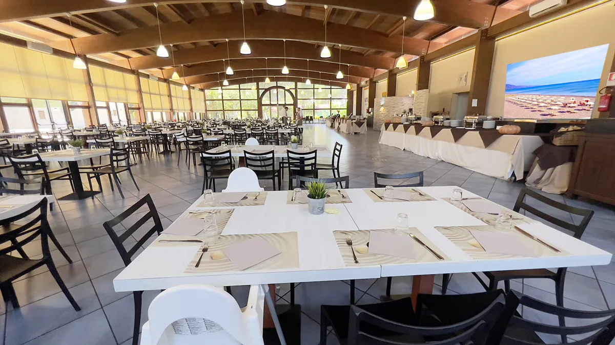 Ampia sala ristorante con tavoli apparecchiati, soffitto in legno e zona buffet