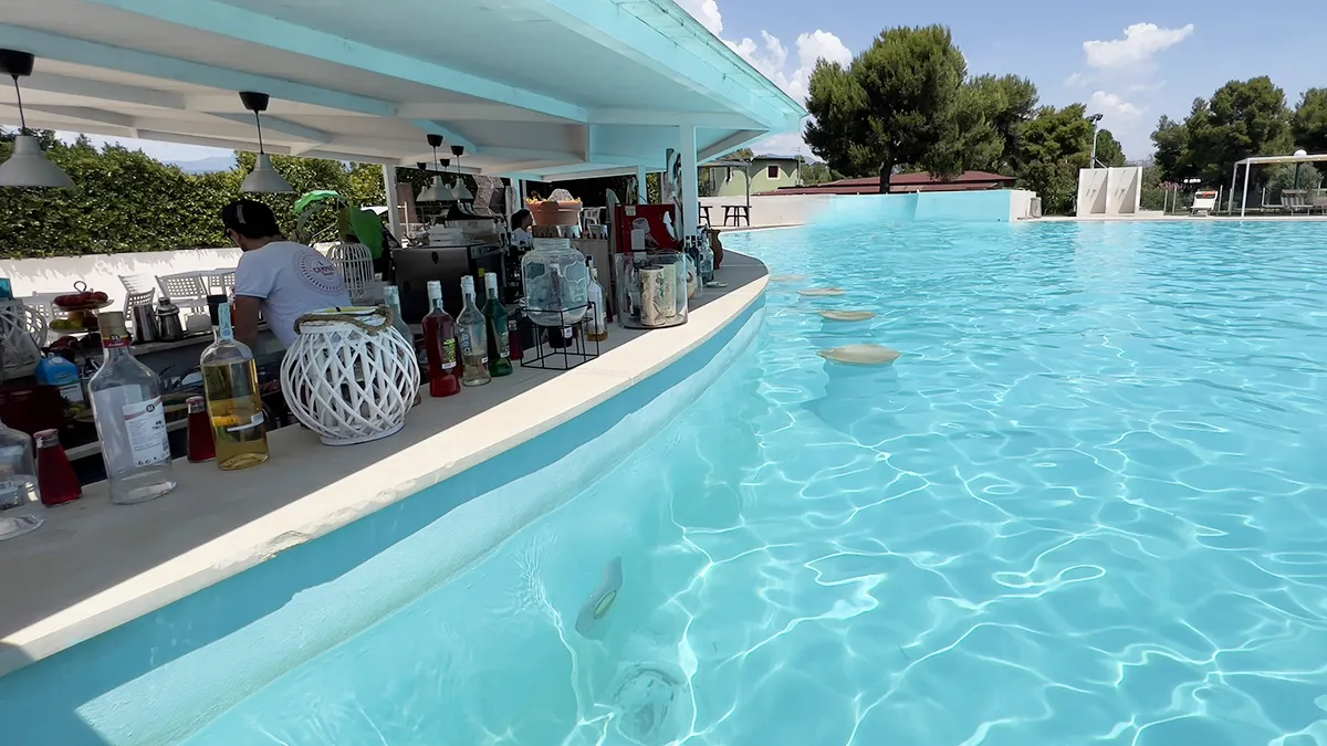 Bar in piscina con bottiglie sul bancone e acqua turchese in primo piano