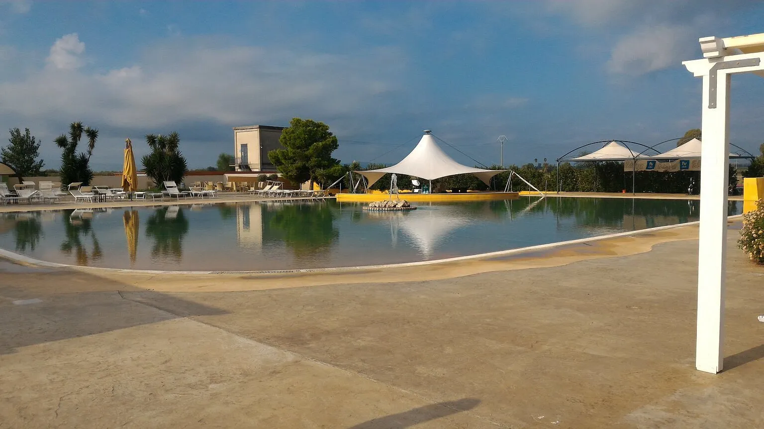 Piscina con fondo sabbiato, gazebo a vela bianca e area solarium