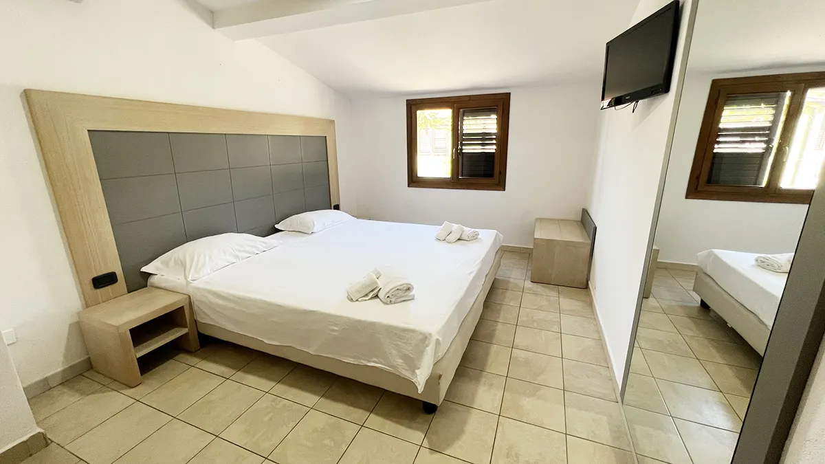 Camera matrimoniale luminosa con letto, TV e finestra con persiane