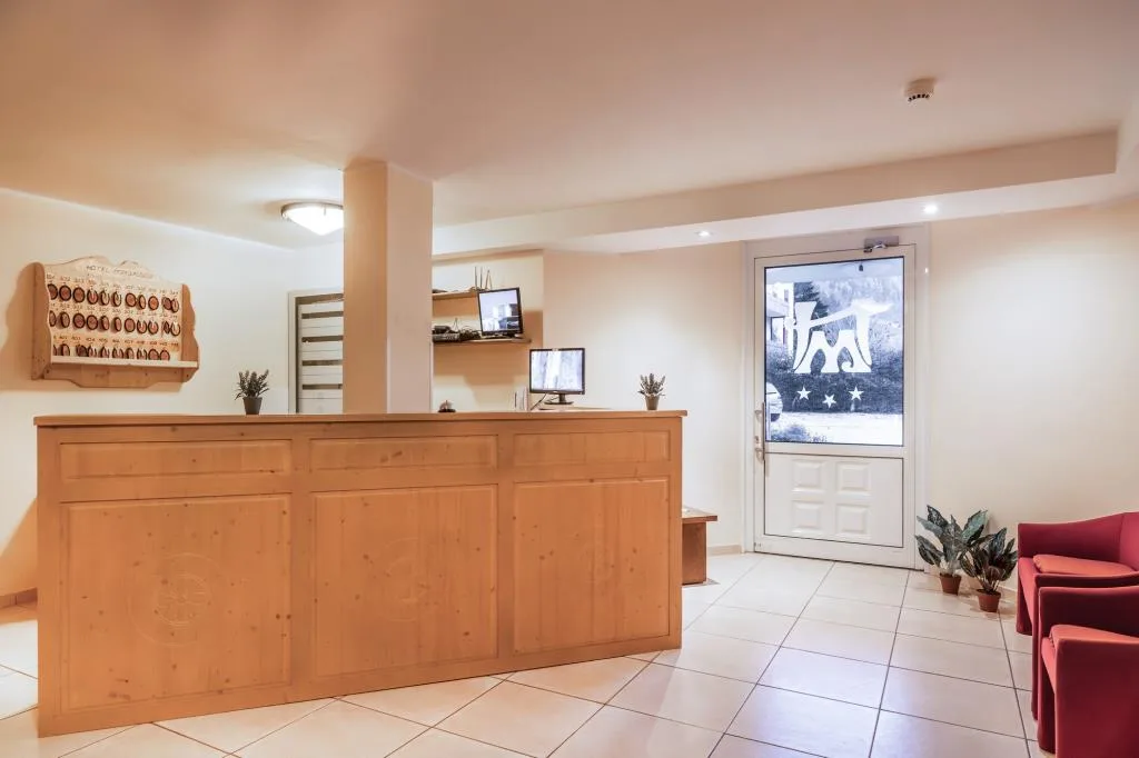 Reception dell'hotel con bancone in legno, poltrone rosse e porta d'ingresso