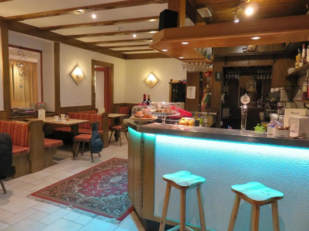 Bar interno dell'hotel con bancone illuminato, sgabelli in legno e zona salotto con sedute rosse