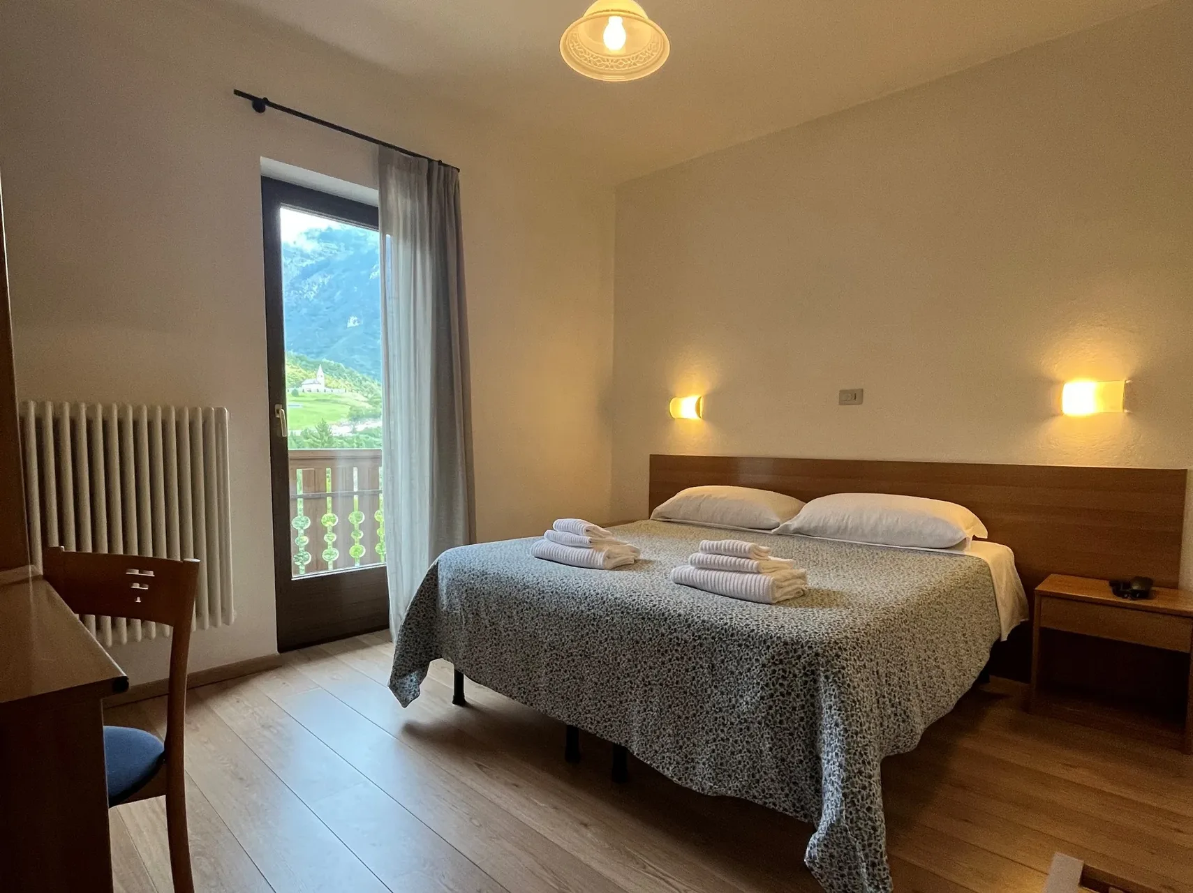 Camera matrimoniale con balcone affacciato sulle montagne e una chiesetta