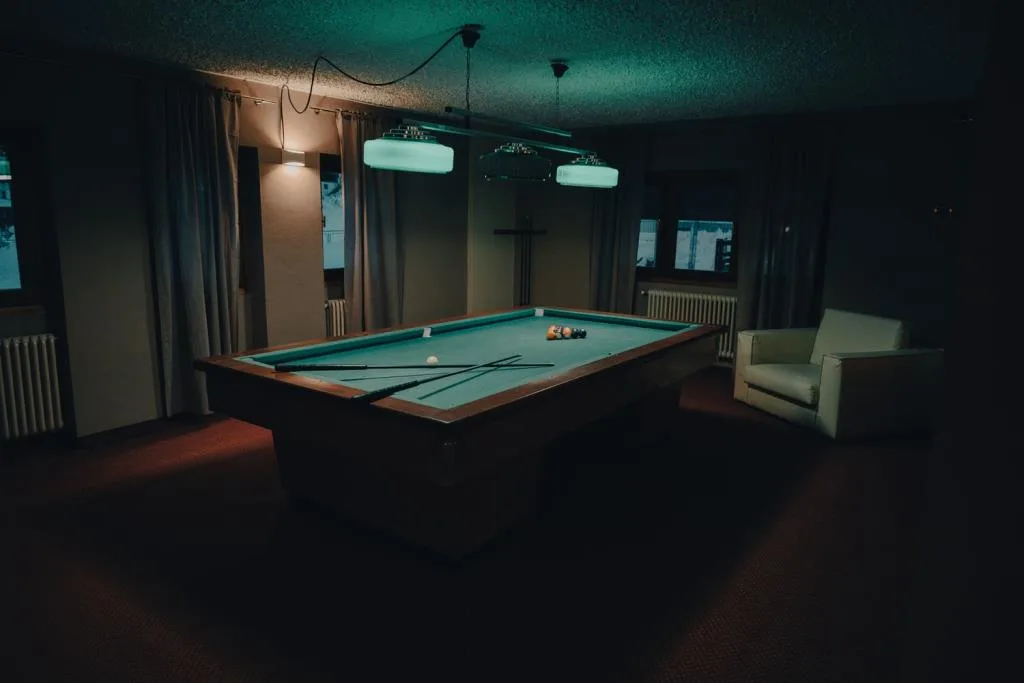 Sala biliardo con tavolo verde e poltrona in penombra