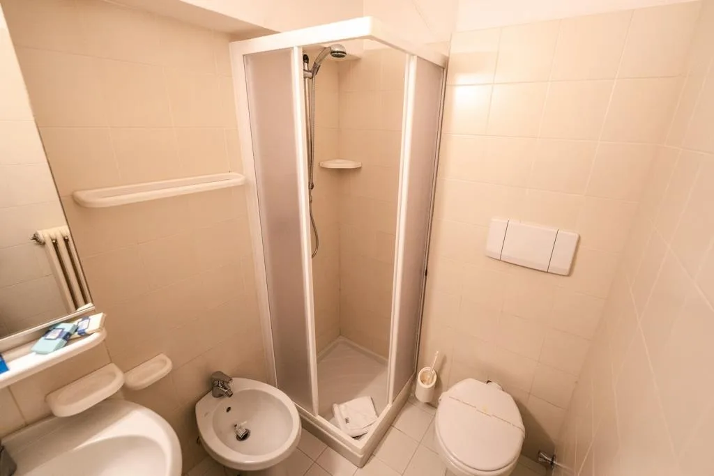 Bagno con doccia ad angolo, bidet e WC, piastrelle chiare