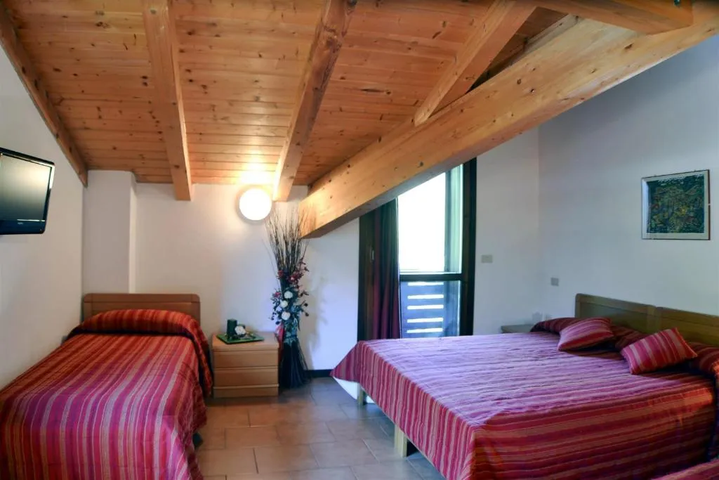 Camera tripla con soffitto travi in legno e copriletti a righe rosse