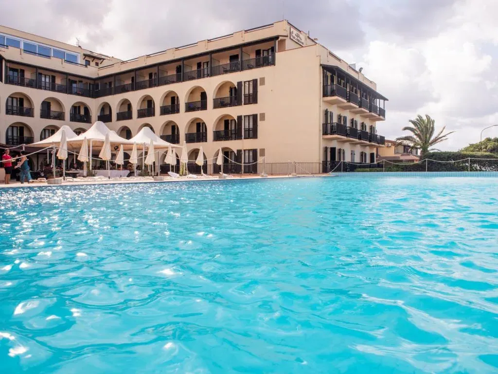 Veduta dell'hotel dalla piscina con acqua turchese e ombrelloni bianchi