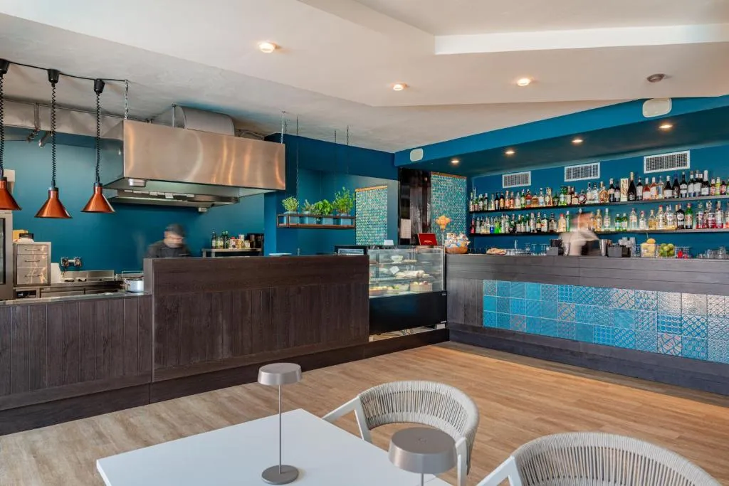 Bar interno con pareti azzurre, banco in legno e ampia selezione di bottiglie