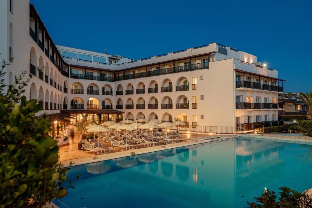 Esterno dell'hotel illuminato di sera con piscina, lettini e ombrelloni