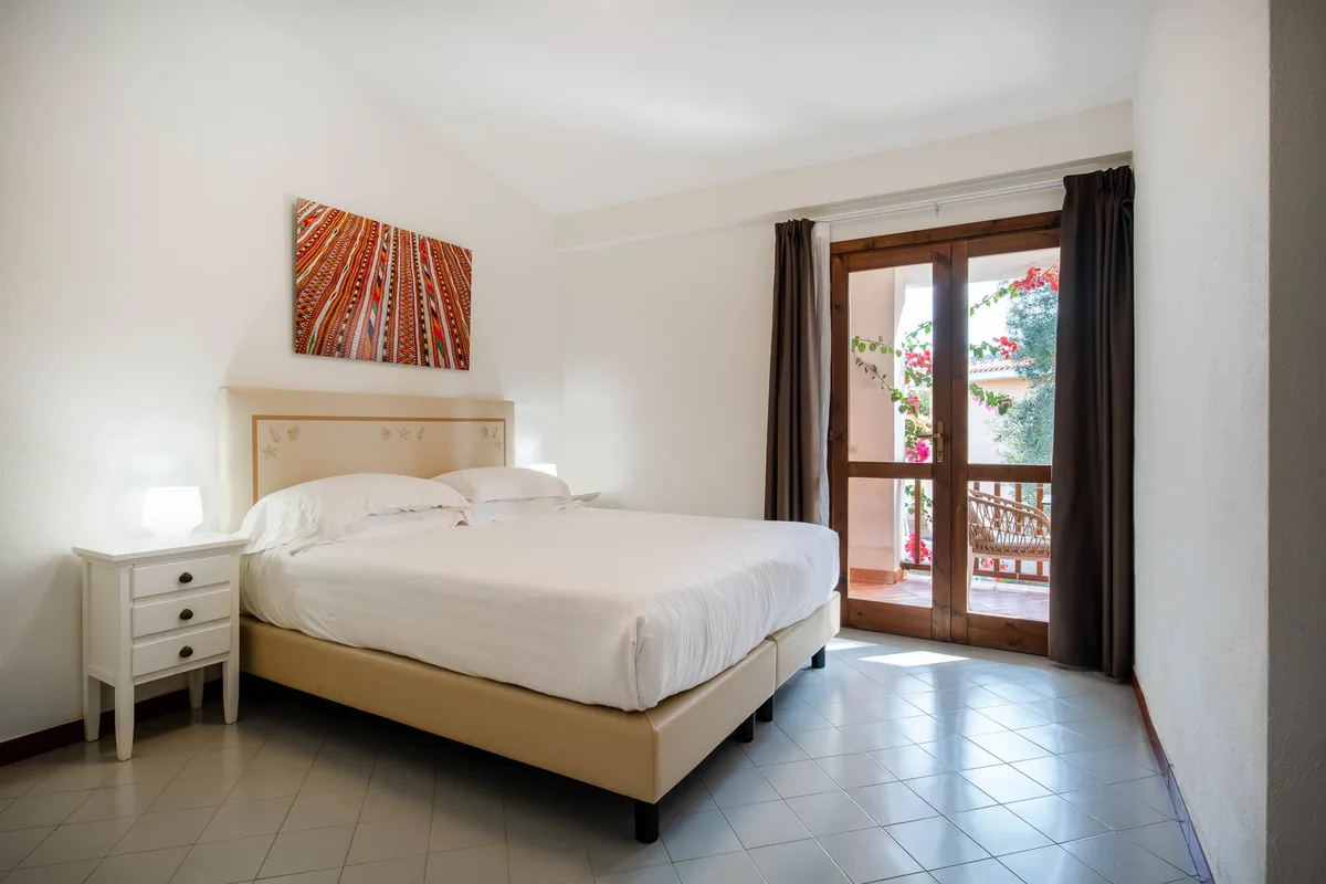 Camera matrimoniale con letto, comodino e porta finestra su terrazza fiorita