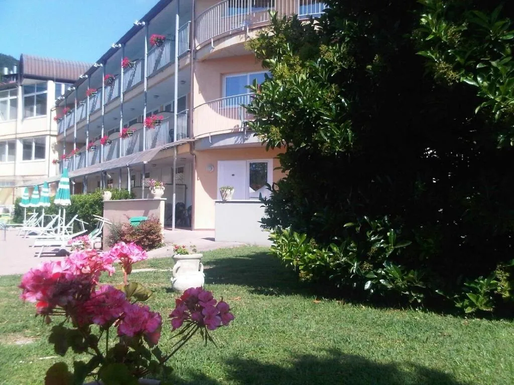 Esterno dell'hotel con balconi fioriti di gerani rossi, giardino verde e fiori rosa in primo piano