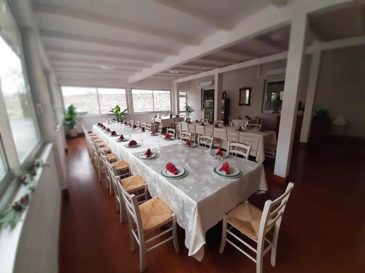 Sala ristorante con lunghi tavoli apparecchiati con tovaglie bianche, tovaglioli rossi e sedie in legno chiaro