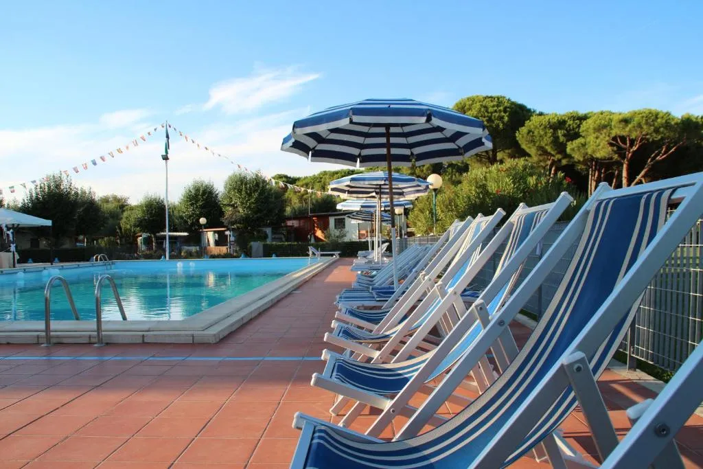 Piscina esterna con lettini e ombrelloni a righe blu e bianche circondata da pini