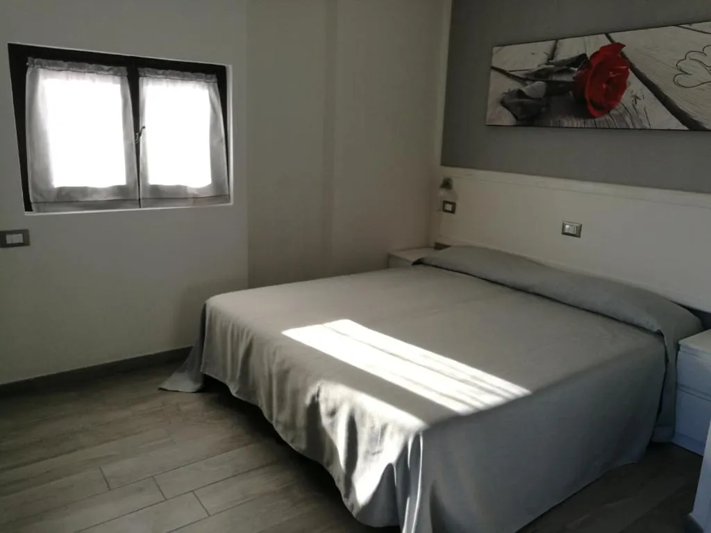Camera da letto luminosa con letto matrimoniale, finestra e quadro con rosa rossa