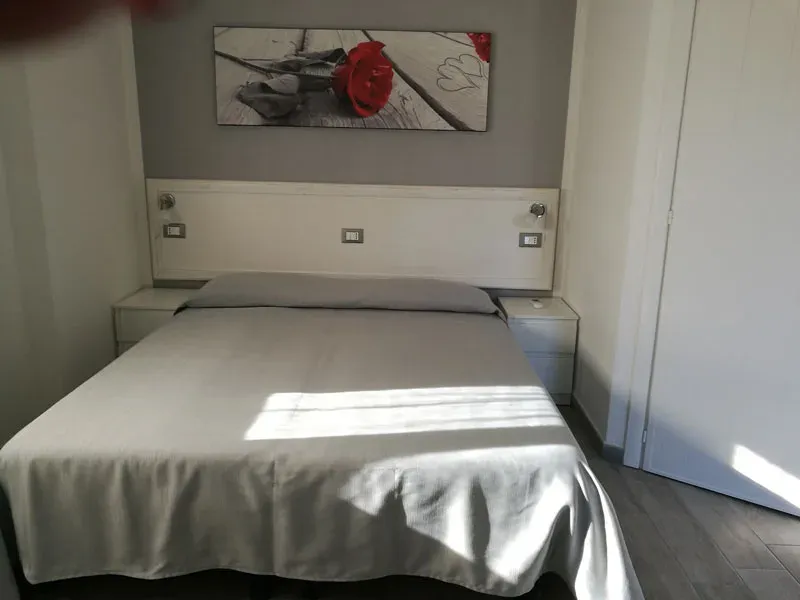 Camera da letto con letto matrimoniale, biancheria grigia e quadro con rosa rossa