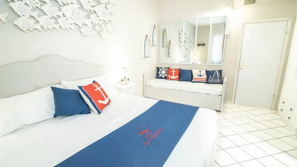 Camera a tema marinaro con letto matrimoniale, divano con cuscini nautici e specchio a parete