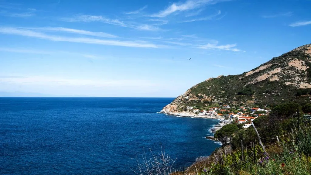 Veduta panoramica della costa con mare blu, montagna e piccolo borgo affacciato sull'acqua