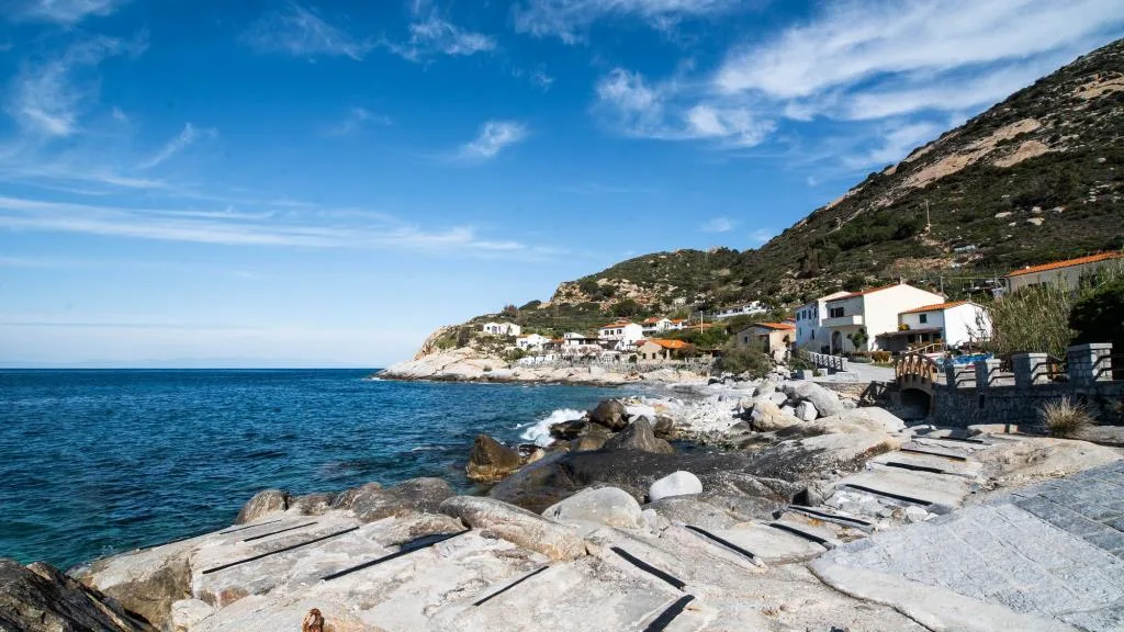 Scogliera rocciosa con mare azzurro e abitazioni bianche sulla costa