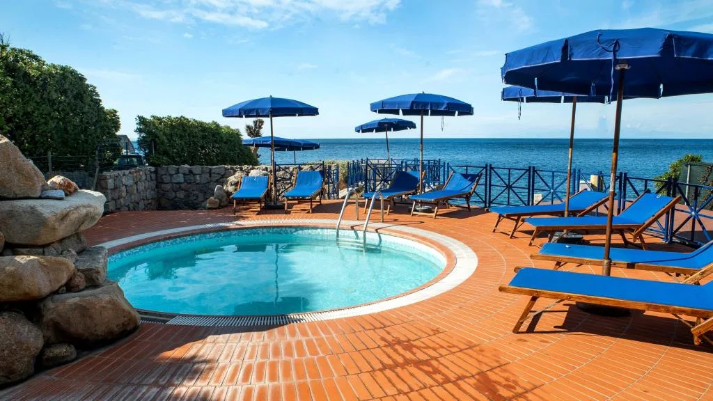 Piscina con pavimentazione in cotto, lettini e ombrelloni blu vista mare