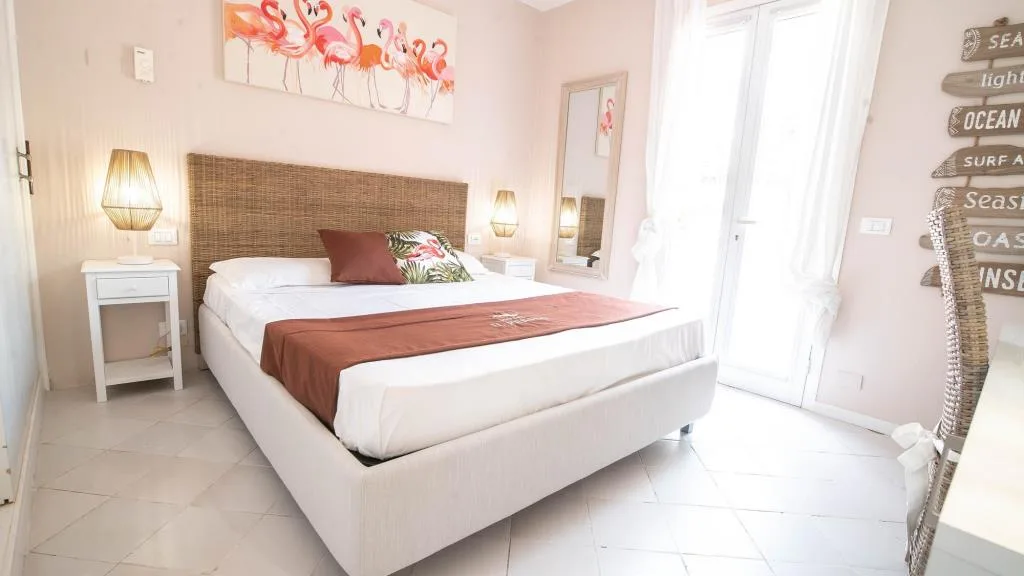 Camera rosa con letto matrimoniale, testiera in rattan e quadro di fenicotteri a parete