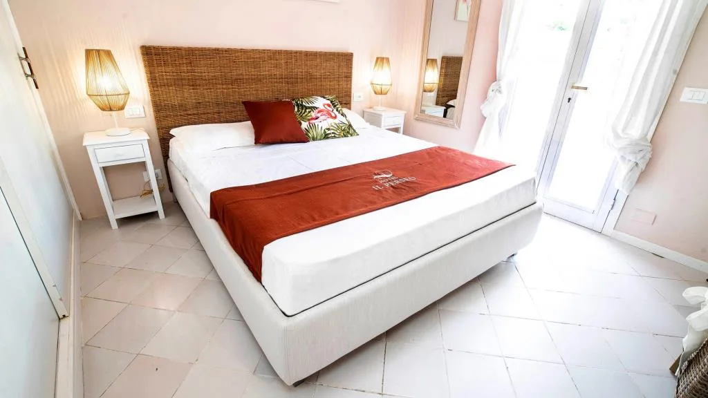 Camera rosa con letto matrimoniale, copriletto color mattone e porta finestra luminosa