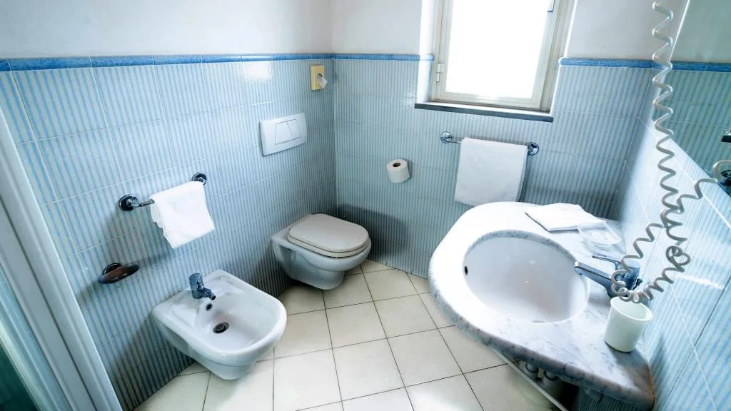 Bagno con piastrelle azzurre, lavabo in marmo, WC e bidet