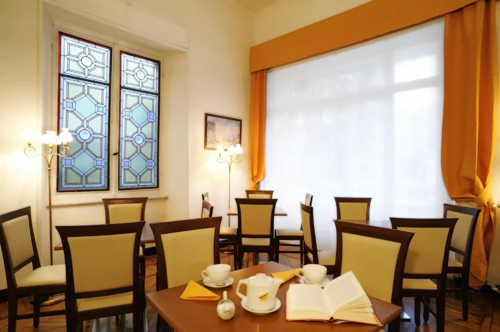 Sala colazione con tavoli in legno, sedie imbottite, vetrata artistica e tazze da tè