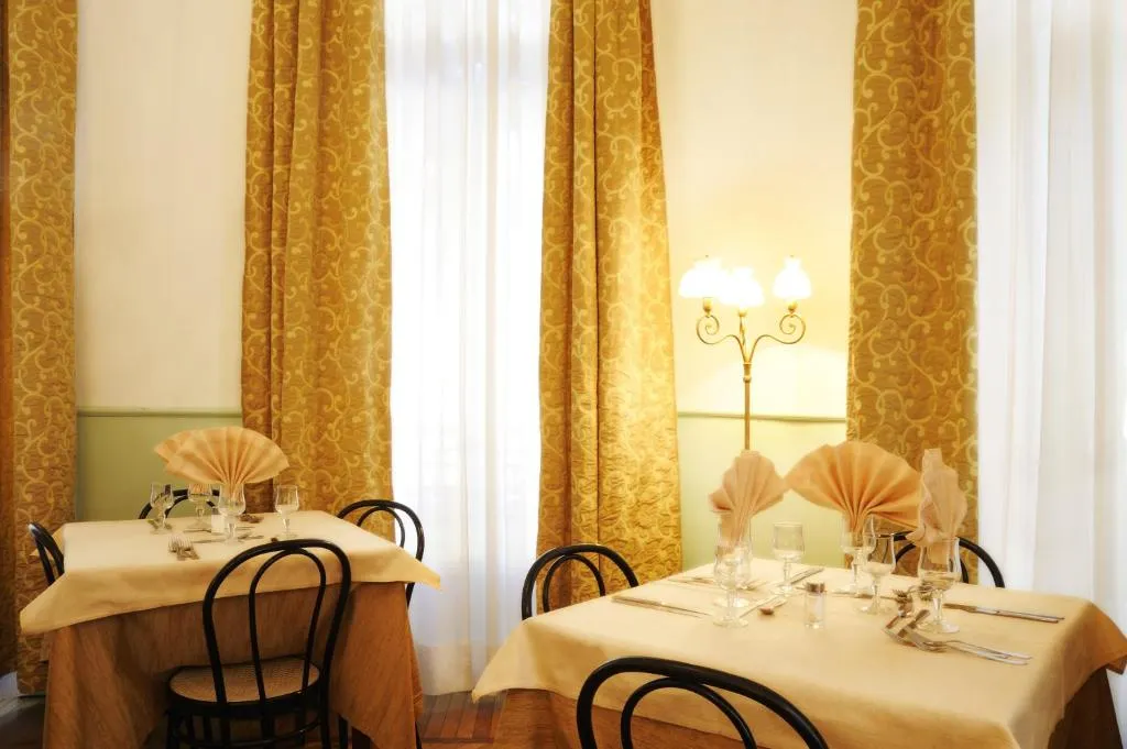 Sala ristorante con tavoli apparecchiati, tovaglioli a ventaglio e tende dorate alle finestre