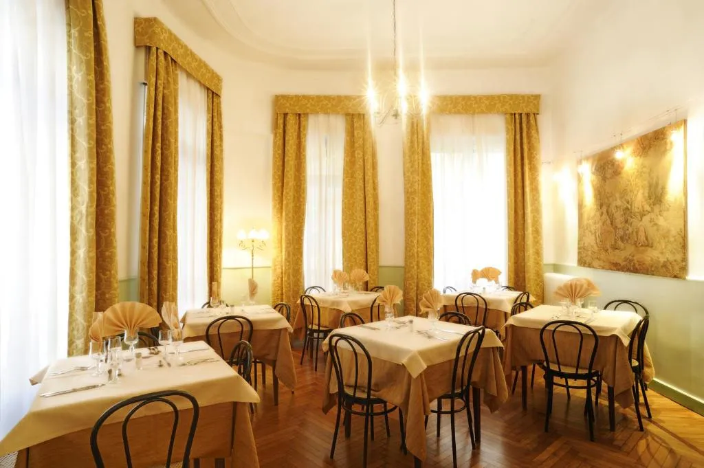 Sala da pranzo con tavoli apparecchiati, sedie nere in stile thonet e arazzo alle pareti