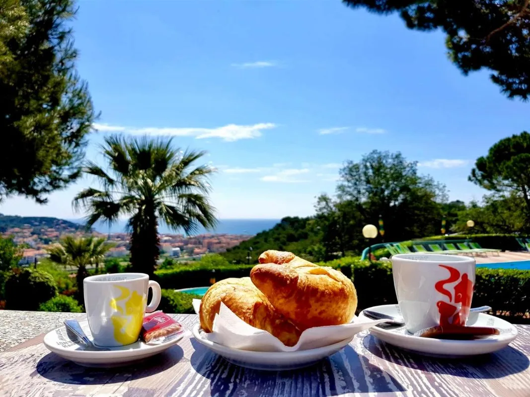 Colazione con cornetto e caffè su tavolo all'aperto con vista mare e palme