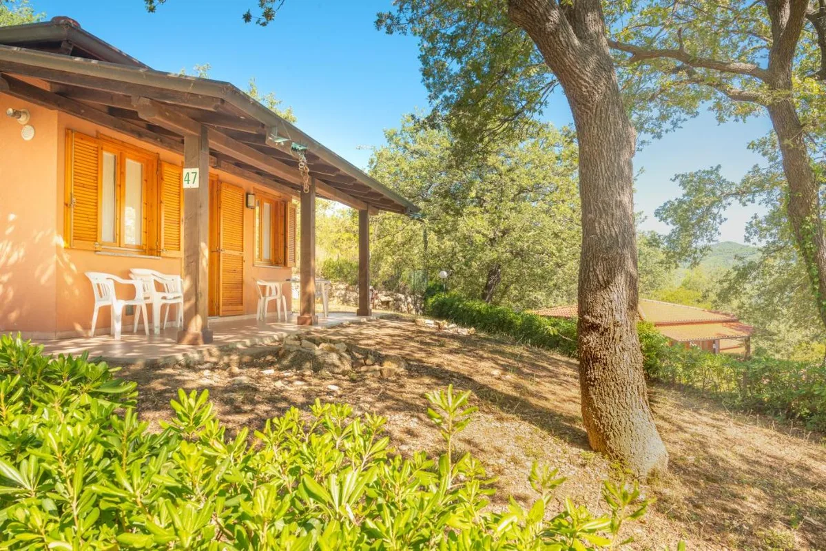 Casetta in muratura con veranda coperta, sedie e tavolo immersa nella natura