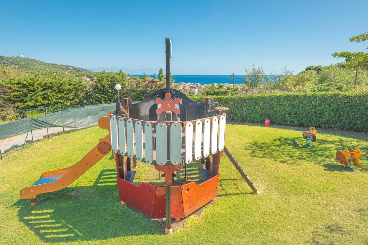 Parco giochi per bambini a forma di nave su prato verde con vista mare
