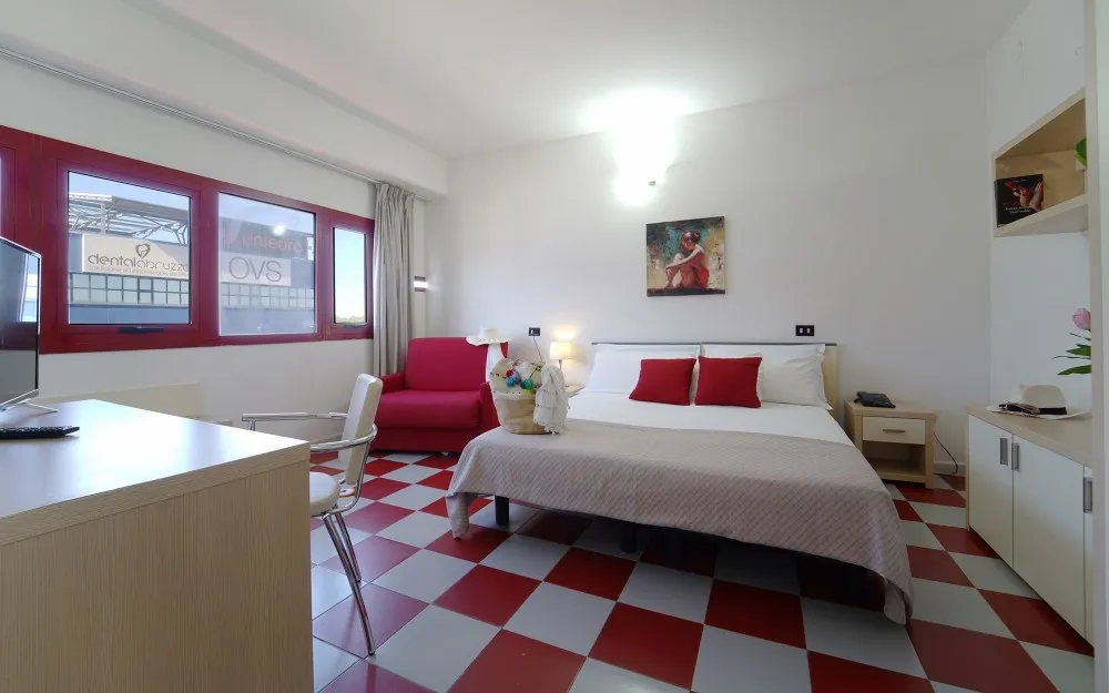 Camera con letto matrimoniale e letto singolo, pavimento a scacchi e finestra con infissi rossi