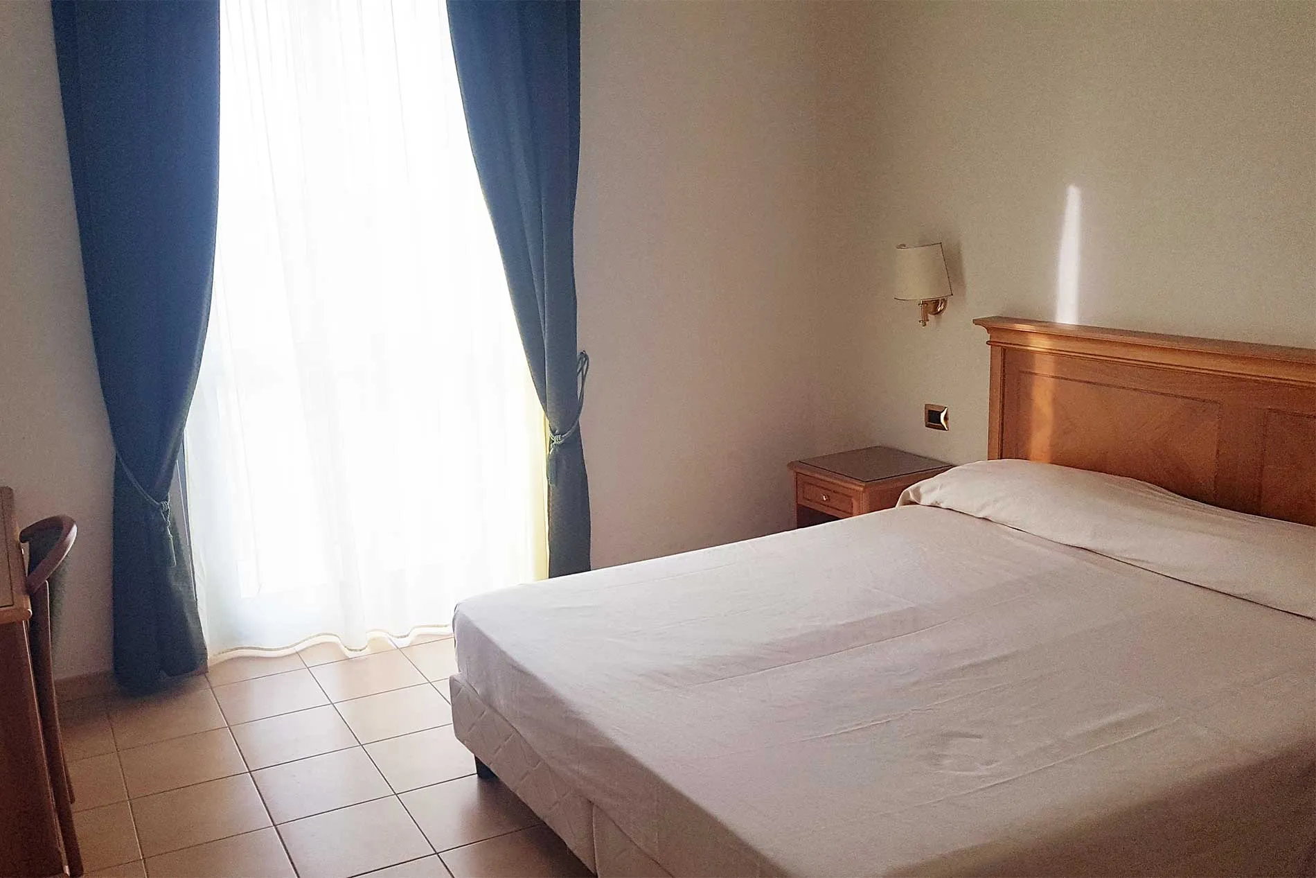 Camera con letto matrimoniale, testiera in legno e tende blu alla finestra