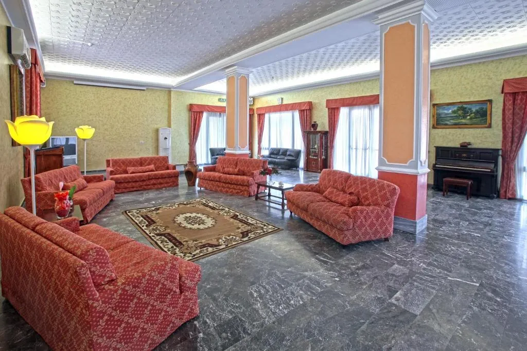 Ampia hall con divani rossi, pavimento in marmo e pianoforte