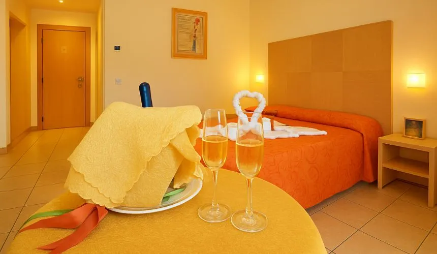 Camera con letto arancione allestita romanticamente con spumante e calici su tavolo