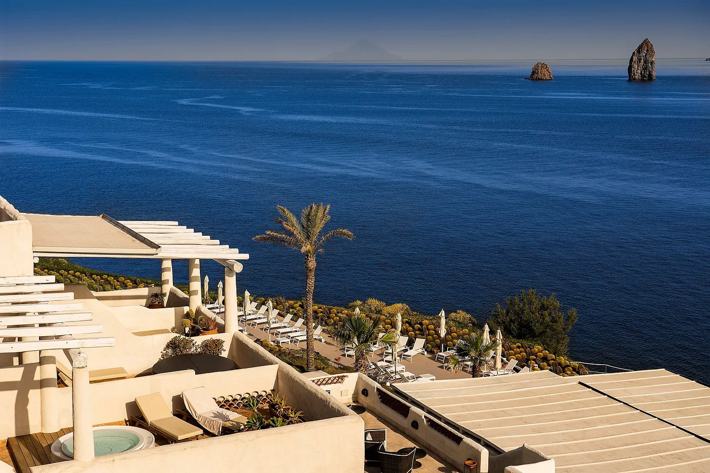 Vista dall'alto delle terrazze dell'hotel con palma e panorama sul mare e i faraglioni