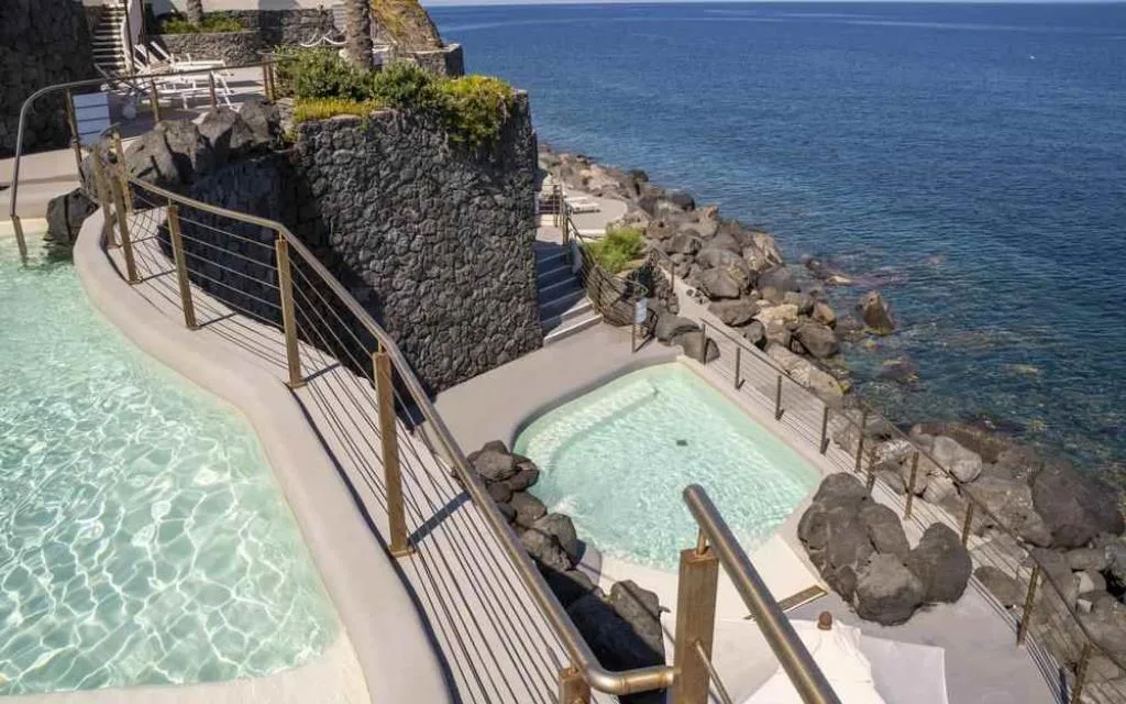 Piscine idromassaggio a picco sul mare con parete in pietra lavica e scogliera
