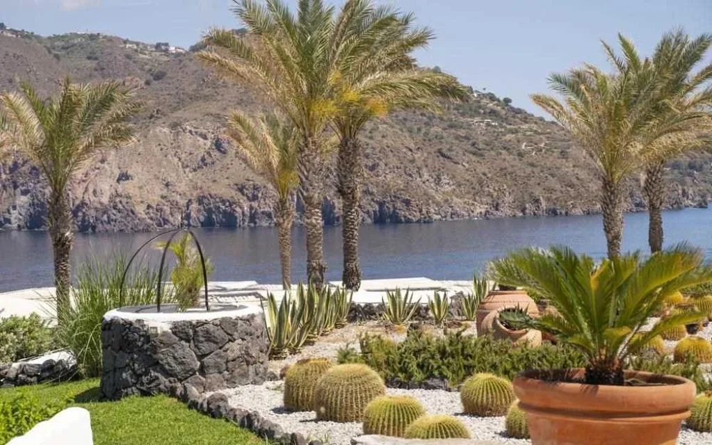 Giardino con palme, cactus e vasi in terracotta affacciato sulla costa rocciosa